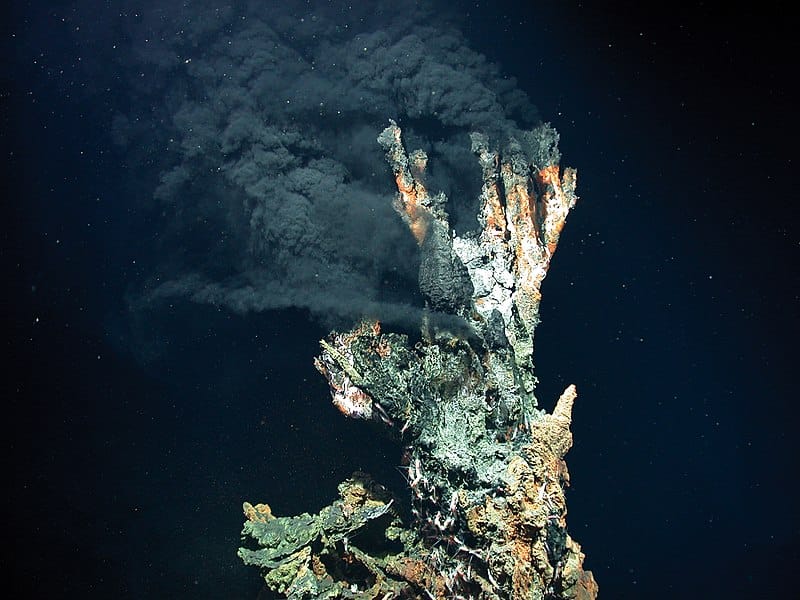 Photo of an active deep sea vent with plumes of black smoke against a nearly black background.