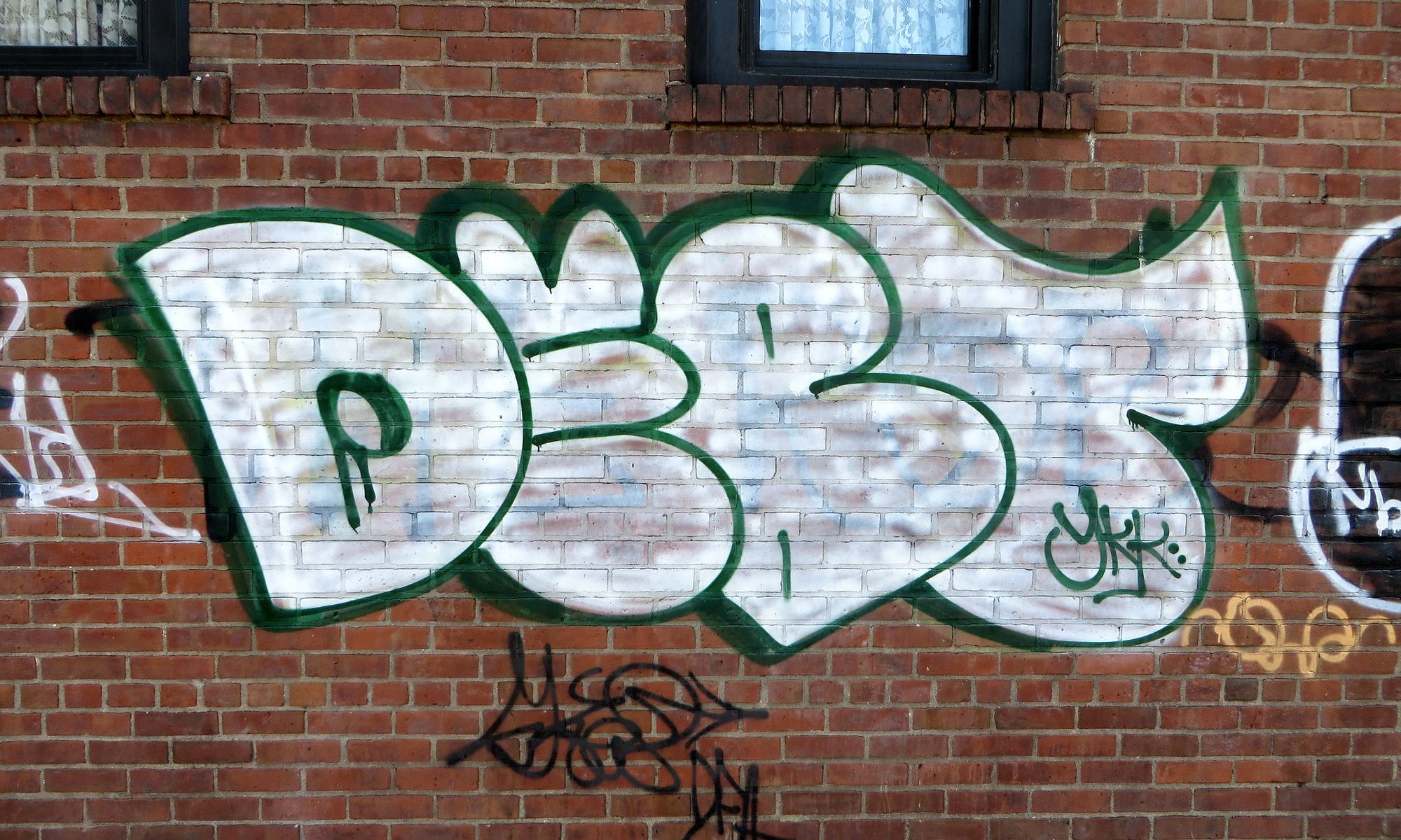 A photo of the word Debt spraypainted on a brick wall: multicolor shading, bubble letters.