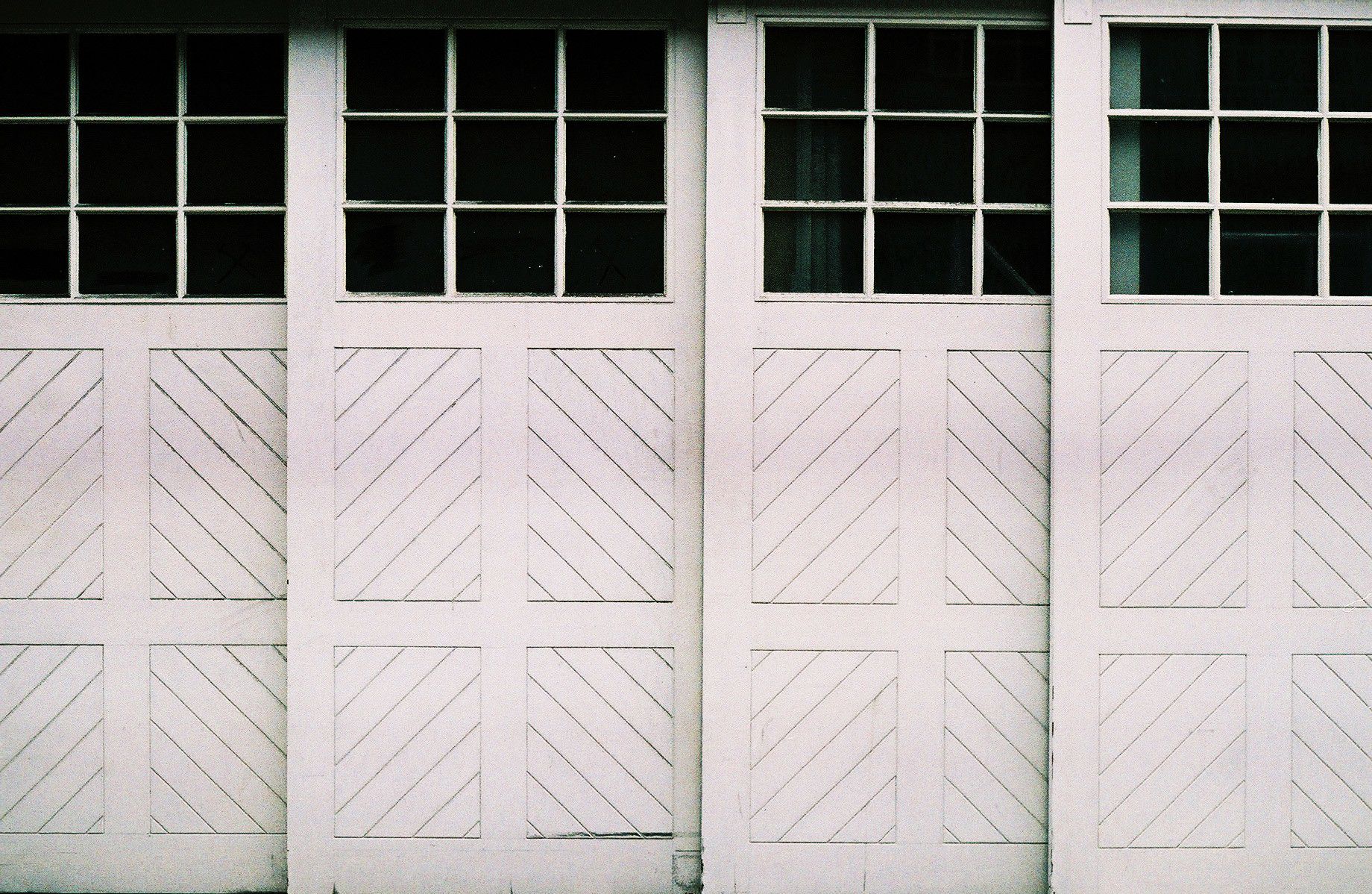 A photo of an older, wooden sliding garage door made of four panels, with windows near the top.